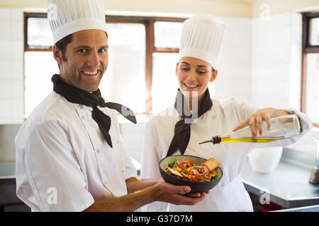 Happy Chef gießt Olivenöl auf Salat Stockfoto