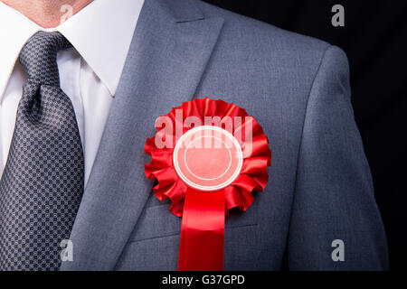 Kopf und Schultern Ansicht des Wahl-Kandidaten tragen eine rote Rosette, vor einem schwarzen Hintergrund. Stockfoto