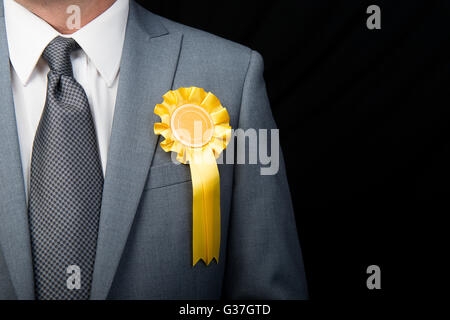 Kopf und Schultern Ansicht des Wahl-Kandidaten tragen eine gelbe Rosette vor einem schwarzen Hintergrund. Stockfoto