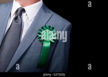 Kopf und Schultern Ansicht des Wahl-Kandidaten tragen eine grüne Rosette vor einem schwarzen Hintergrund. Stockfoto