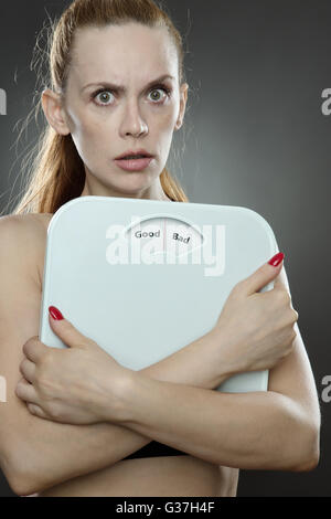 Frau im Studio gedreht, skaliert low Key Beleuchtung Gewicht halten mit den Worten gut schlecht auf der Waage Platte gedruckt Stockfoto