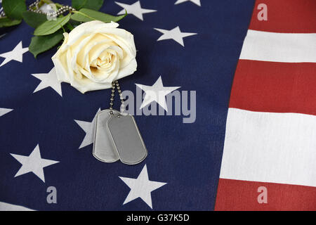 Einzelne weiße Rose mit militärischen Hundemarke auf amerikanische Flagge. Stockfoto