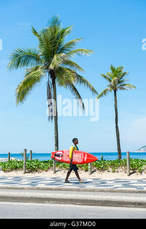 RIO DE JANEIRO - 28. Februar 2016: Carioca brasilianischen Mann trägt Surfbrett entlang der Ipanema Beach Boardwalk. Stockfoto