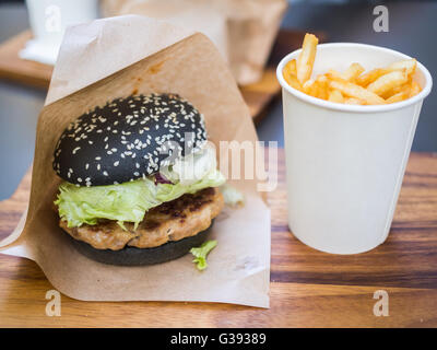 Schwarz-Burger mit pikanter Sauce und Pommes Frites auf Tablett aus Holz Stockfoto
