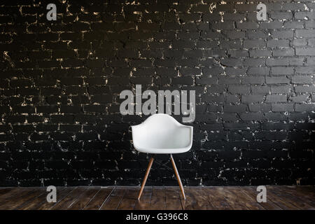 Weißer Stuhl stehend im Raum auf braunem Holzboden über schwarze Ziegelmauer Stockfoto