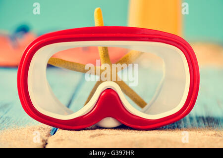 Nahaufnahme von roten und weißen Tauchmaske auf einem Haufen Sand und einen gelben Seestern, platziert auf einer rustikalen blau Holzoberfläche Stockfoto