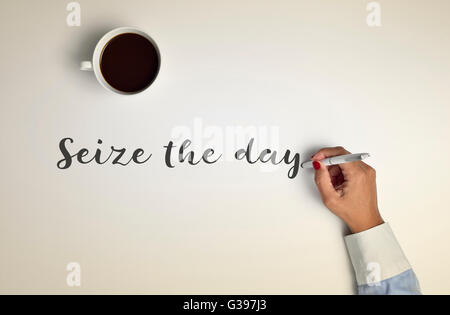 High-Angle Shot von einer Tasse Kaffee auf einer Off-White-Oberfläche und eine junge Frau, die Abfassung des Textes nutzen Sie den Tag mit einem Stift Stockfoto