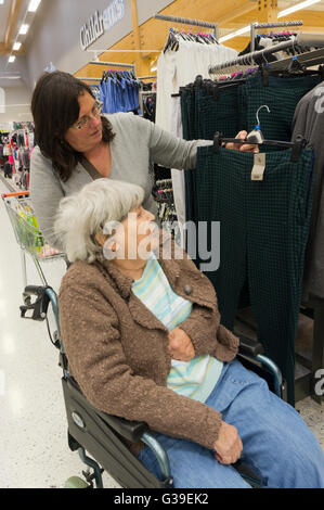 Ältere Frau im Rollstuhl und ihre Pfleger oder Assistent Einkauf für die Kleidung. Stockfoto
