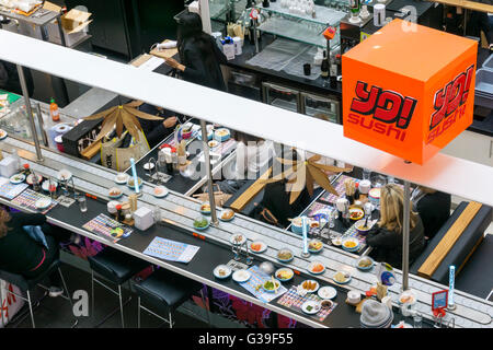 Menschen essen japanisches Essen bei einer Filiale der Yo! Sushi in Bromley mit Schüsseln mit Essen vorbei am laufenden Band. Stockfoto