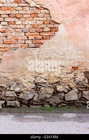 Ziegelwand mit angeschlagenen Putz, Steinfundament und Asphaltstraße Stockfoto