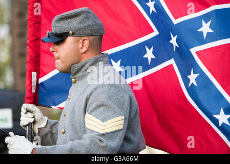 ARLINGTON Virginia / ARLINGTON, Virginia — Eine Person, die als konföderierter Soldat aus dem Amerikanischen Bürgerkrieg gekleidet ist, hält eine Konföderierte Schlachtflagge, auch bekannt als Southern Cross. Die graue Uniform des Soldaten hat goldene Knöpfe, gelbe Chevrons, die den Rang anzeigen, einen Kepi und weiße Handschuhe, die zur Kleidung der Konföderierten Armee passen. Diese Bilder werden häufig bei historischen Nachstellungen oder Gedenkveranstaltungen gesehen. Die Confederate Battle Flag ist ein historisch bedeutendes und oft kontroverses Symbol der Konföderierten Staaten von Amerika. Diese Szene spielt in Arlin Stockfoto