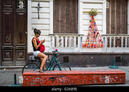 Eine junge Dame mit ihrem Fahrrad überprüft ihr Handy in Montevideo, Uruguay, Südamerika. Stockfoto