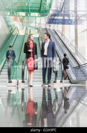 Corporate Geschäftsmann und Geschäftsfrau unter Rolltreppen in modernen Lobby sprechen Stockfoto