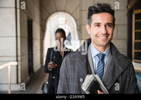 Lächelnd corporate Geschäftsmann mit Zeitung und Handy im Kreuzgang Stockfoto