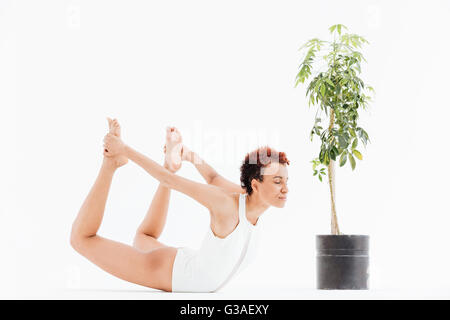Ziemlich junge Afroamerikanerfrau trainieren und üben von Yoga in der Nähe kleiner Baum im Topf auf weißem Hintergrund Stockfoto