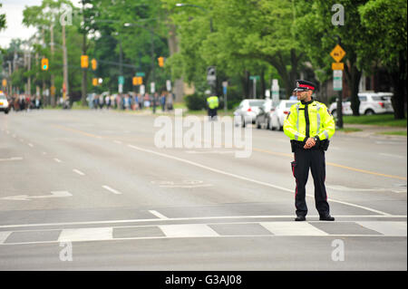 Ein Polizist steht auf der Straße in London, Ontario, während eine Militärparade hinter ihm stattfindet. Stockfoto