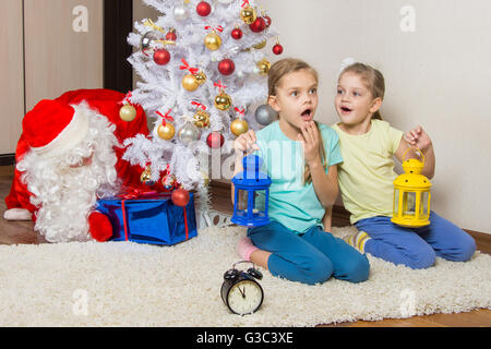 Zwei Mädchen mit Taschenlampen träumen von Geschenken auf Silvester Nacht, und der Weihnachtsmann, Geschenke unter dem Weihnachtsbaum Stockfoto