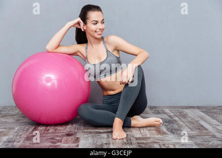 Junge schöne Fitness Mädchen sitzen mit pinkfarbenen Ball auf grauem Hintergrund isoliert Stockfoto