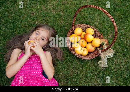 Kleines Mädchen auf Gras- und Essen Apfel liegen Stockfoto