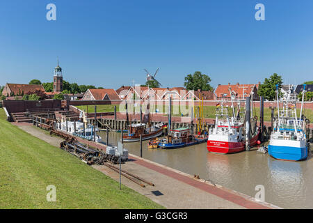 Fischkutter im Hafen von Ditzum, Kirchturm und Mühle im Hintergrund, Ditzum, Ostfriesland, Stockfoto