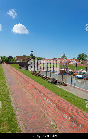 Strandpromenade auf dem Deich, Fischkutter im Hafen von Ditzum, Kirchturm und Mühle im Hintergrund, Ditzum, Ostfriesland, Stockfoto