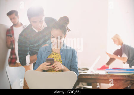 Junger Mann und Frau SMS mit Handy im Büro Stockfoto