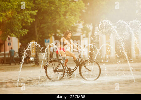 Junge Frau reist mit dem Fahrrad durch einen Brunnen Stockfoto