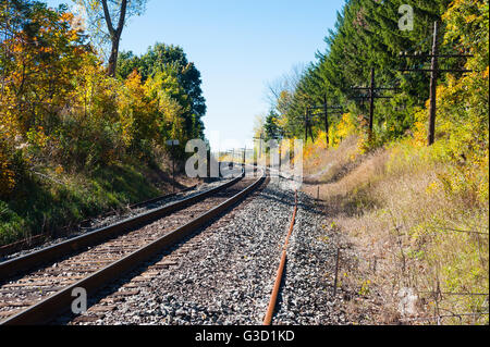 Schienen Sie auf Kiesbett geschwungene links durch Bäume im Herbst, mit Telegrafenmasten auf rechten Seite. Stockfoto