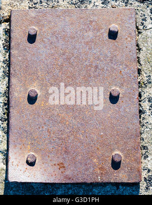 Schwere verrostet Stahlplatte mit sechs Schrauben mit Betonoberfläche im Hintergrund und kurze Schatten. Stockfoto