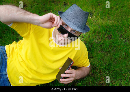 Mann trägt einen Hut mit dem Telefon auf dem Rasen liegend Stockfoto