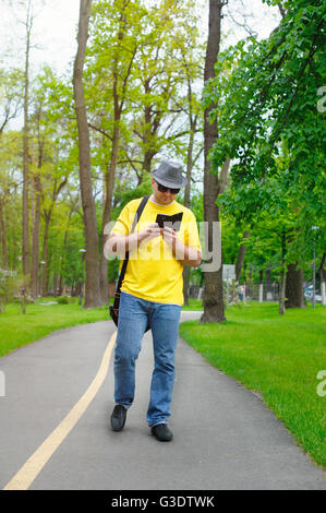 glücklicher Mann mit Hut, gelben T-shirt und Telefon ist im Park spazieren. Stockfoto