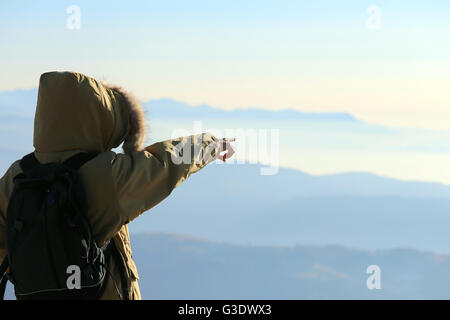 junge Forscher mit Winterjacke mit Kapuze und schwarzen Rucksack zeigt den Horizont von oben die Gipfel der Berge Stockfoto