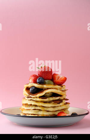 Pfannkuchen mit Beeren auf Platte vor rosa Hintergrund Stockfoto