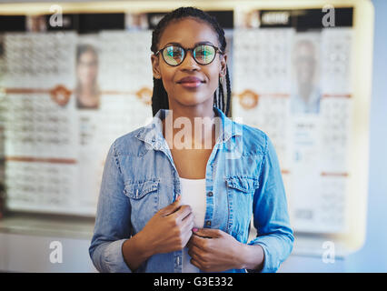 Einzelne glücklich schwarze Frau mit zuversichtlich Ausdruck zentriert im Rahmen mit neuen Gläsern in Vision Care Shop Stockfoto