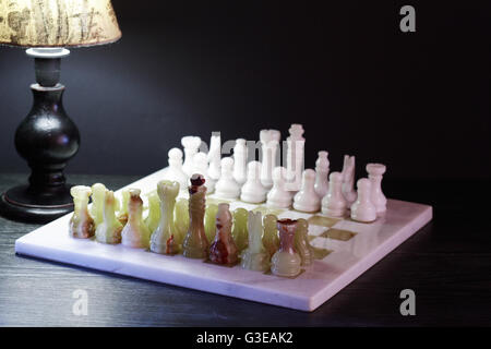 Satz von Schachfiguren aus Onyx an Bord in der Nähe von Schreibtischlampe gemacht Stockfoto
