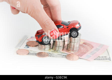 Frau Hand schob ein Spielzeugauto über einen Stapel von Münzen Stockfoto