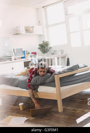 Junger Mann mit auf Bett mit Laptop in Wohnung Stockfoto