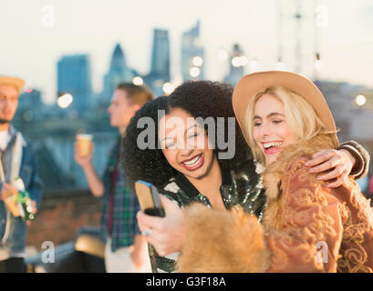 Junge Frauen, die die Selfie auf Dachterrasse Party lachen Stockfoto