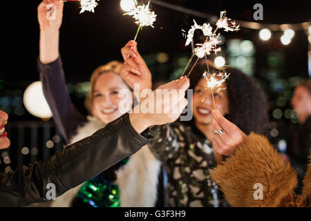 Junge Frauen, die auf dem Dach Partei Wunderkerzen winken Stockfoto