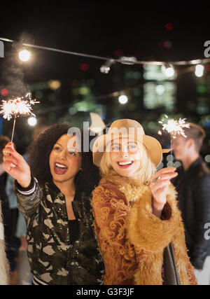 Junge Frauen, die auf dem Dach Partei Wunderkerzen winken Stockfoto