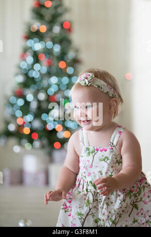 Babymädchen vor Weihnachtsbaum mit Geschenken und Dekorationen Stockfoto