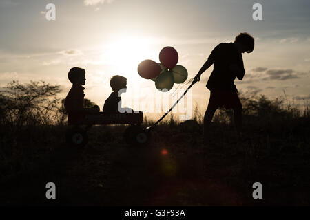 Drei Jungs in der Silhouette spielt mit Cart auf Hügel Stockfoto