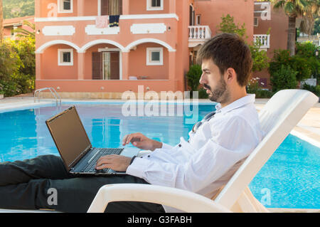 Junge Bussines Mann arbeitet auf Laptop am Pool Stockfoto