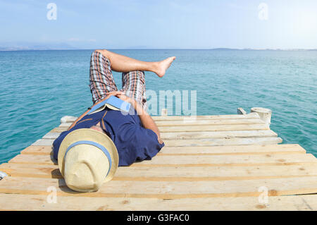 Mann liegt auf dem Dock mit einem Buch. Sommer-Urlaub-Entspannung Stockfoto