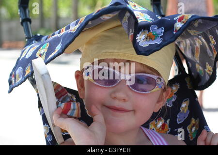 Kleines Mädchen, ein Kind unter einem Vordach in Ihrem Buggy in der Sonne trägt ein Bandana und Sonnenbrille auf ihre Ferien, Urlaub, USA Kinderwagen sun Sicherheitskonzept Stockfoto