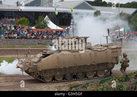 Bovington, Dorset, UK. 25. Juni 2016. Tankfest militärische zeigen. Britische Armee Krieger amoured Personal Carrier mit Darstellung von Rauch und Armee Personal vor den wichtigsten Fans in der Arena Tankfest. Panzermuseum im Hintergrund. Stockfoto