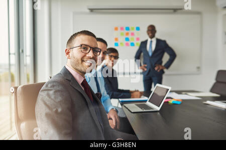Gruppe von vier schwarzen, hispanischen und kaukasischen junge professionelle Erwachsene in einer Besprechung in ihrem Büro in der Nähe von großen Bord teilweise co Stockfoto
