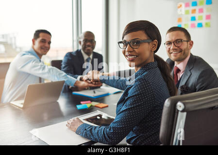 Erfolgreichen afroamerikanischen Teamleiter drehen, um in die Kamera zu Lächeln, als ihr multiethnischen Team von Führungskräften Links Hände über Stockfoto