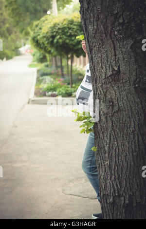 Schwangere Frau in einem Versteck hinter dem Baum im Park. Schwangerschaft-Konzept. Stockfoto