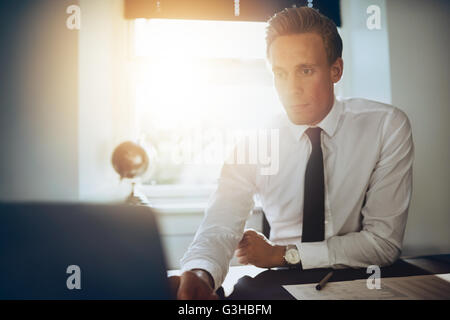 weiße männliche executive Business Mann arbeitet an seinem Laptop sitzt an seinem Schreibtisch in ein weißes Hemd und schwarze Krawatte Stockfoto